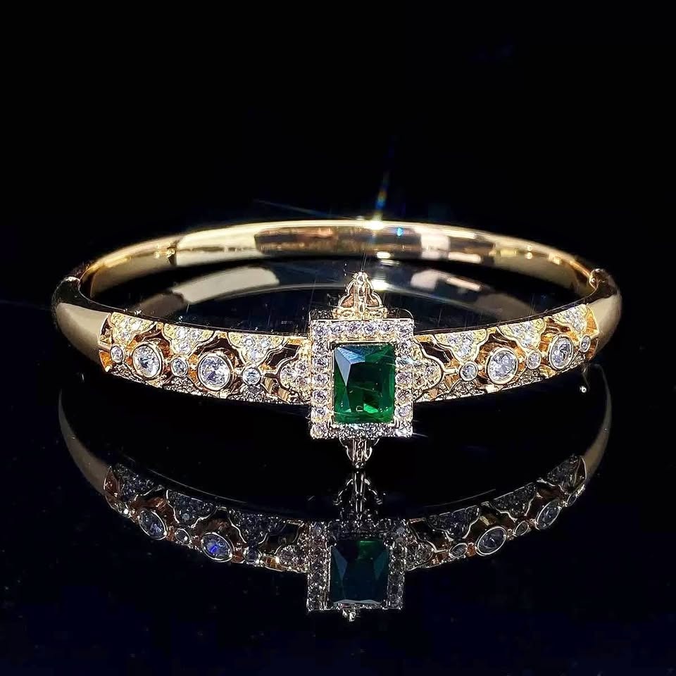Gold-toned bangle bracelet with a central emerald-cut green zirc