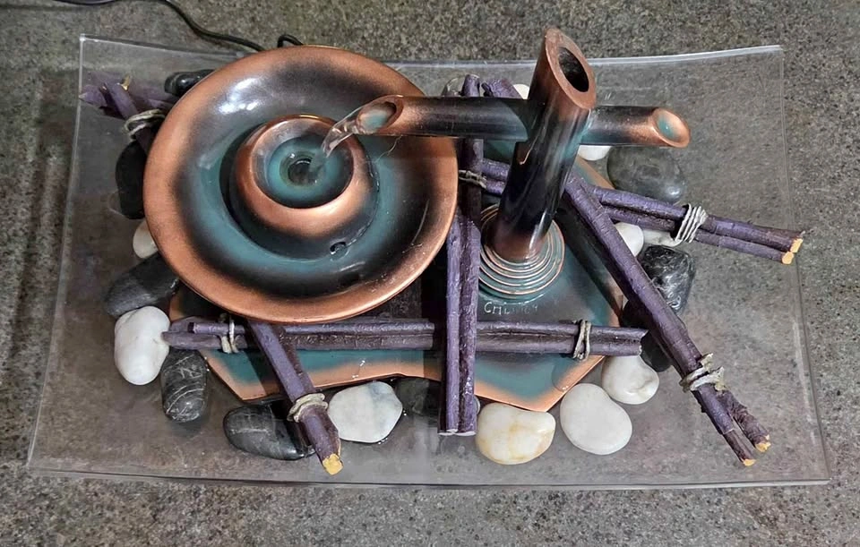 Zen tabletop water fountain on bed of river stones, bundle ties