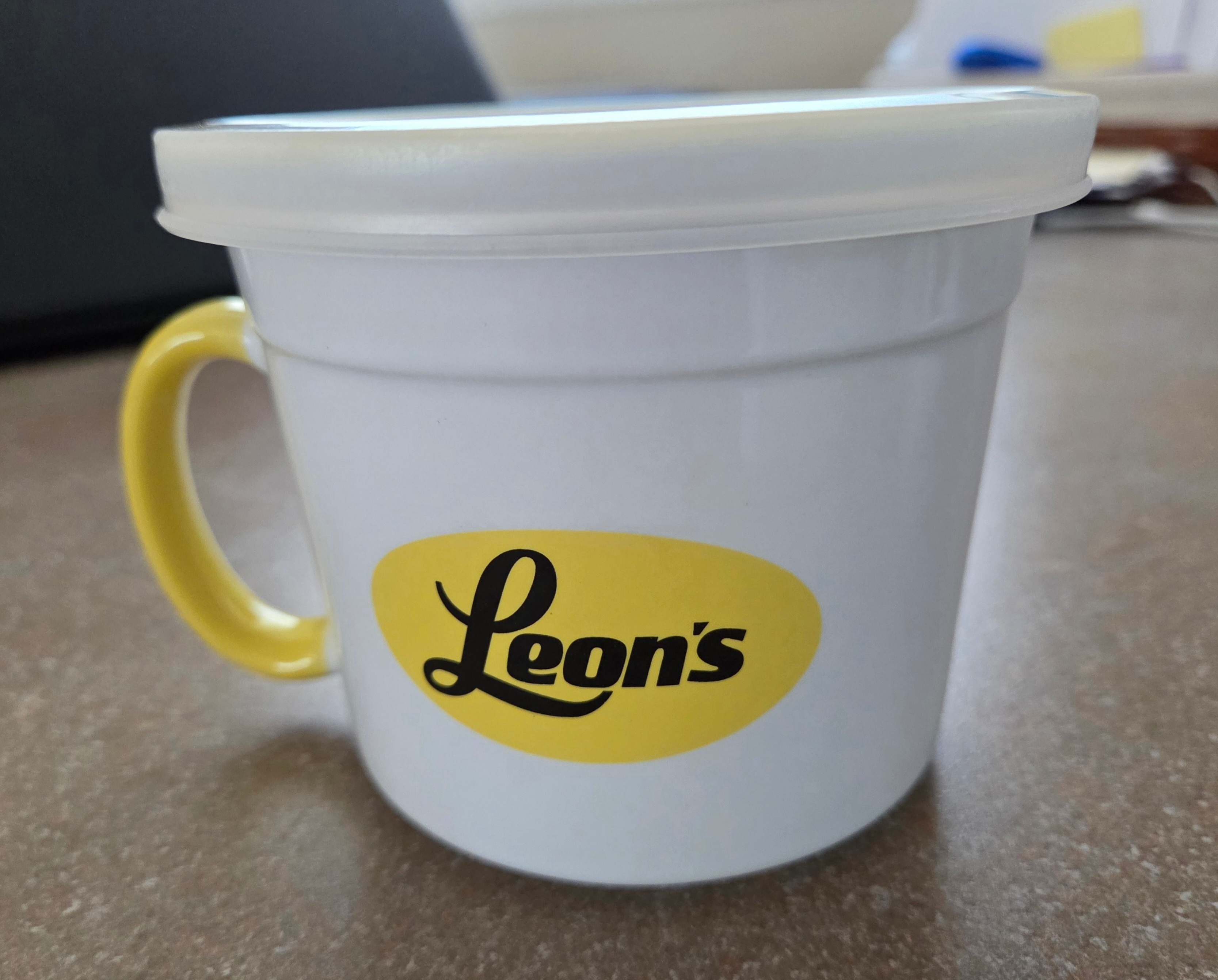 Leon’s brand mug/container w/ yellow handle & white plastic lid.