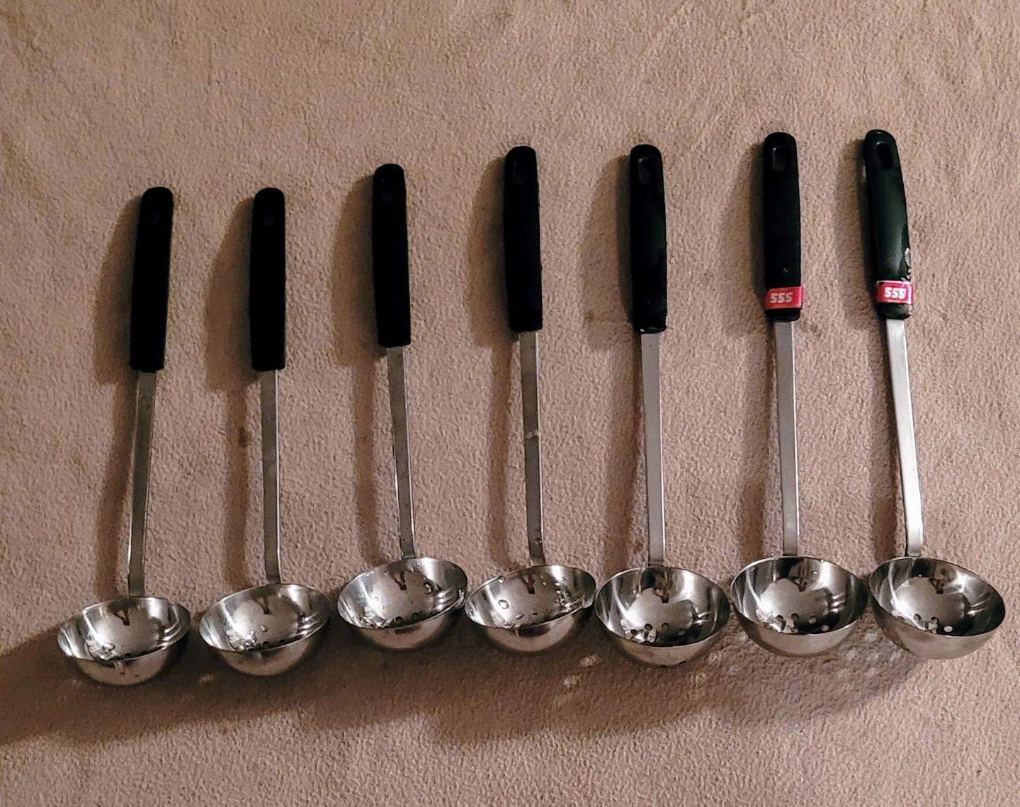 Seven Stainless Steel Slotted Spoons with Black Handles thumbnail