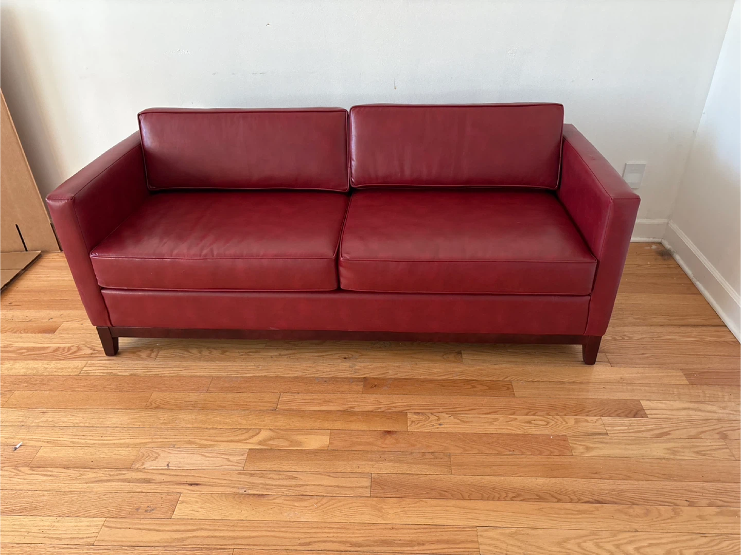 Small red leather couch . Has a wood frame .