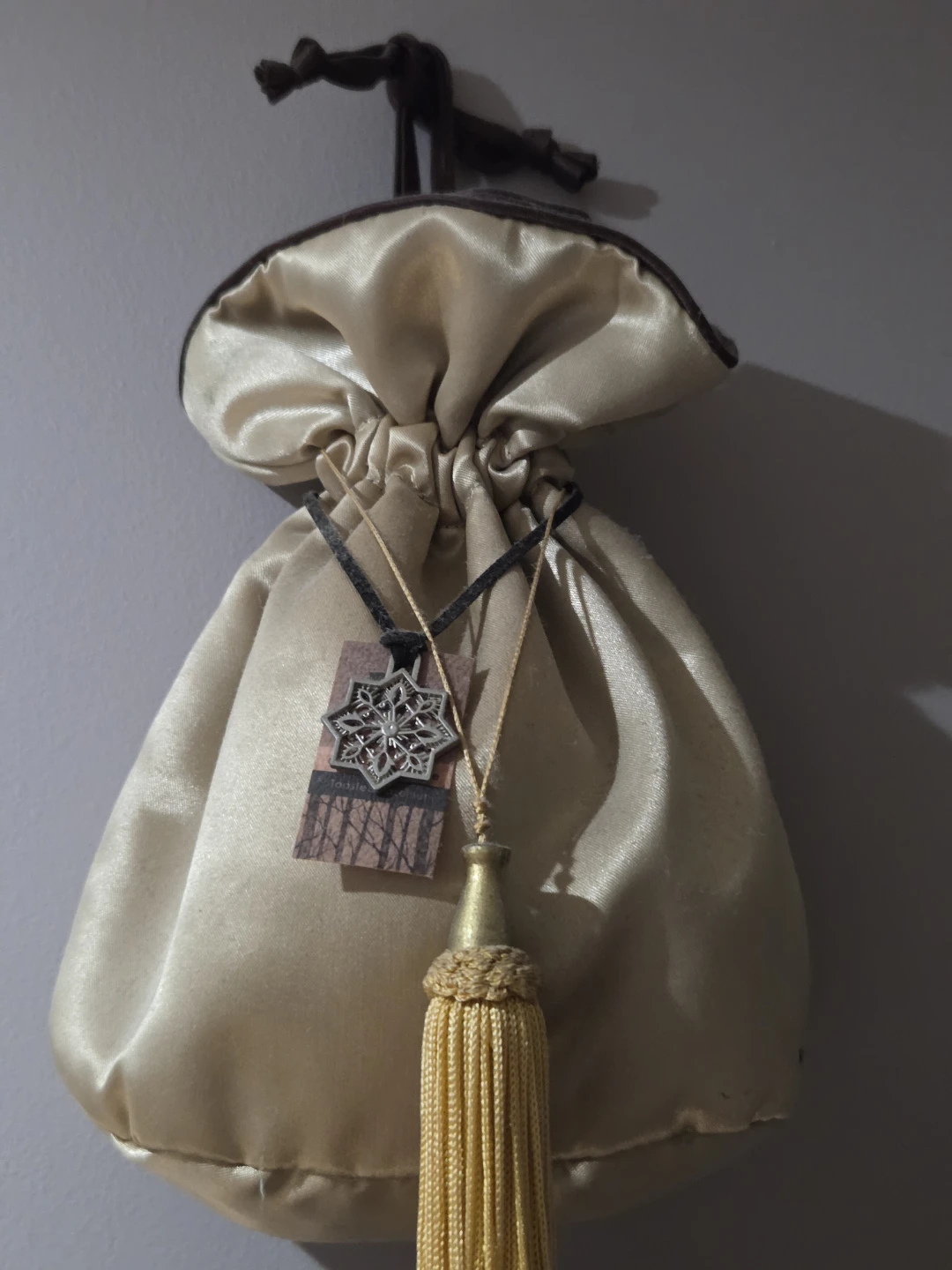 Gold satin drawstring bag with tassel and charm
