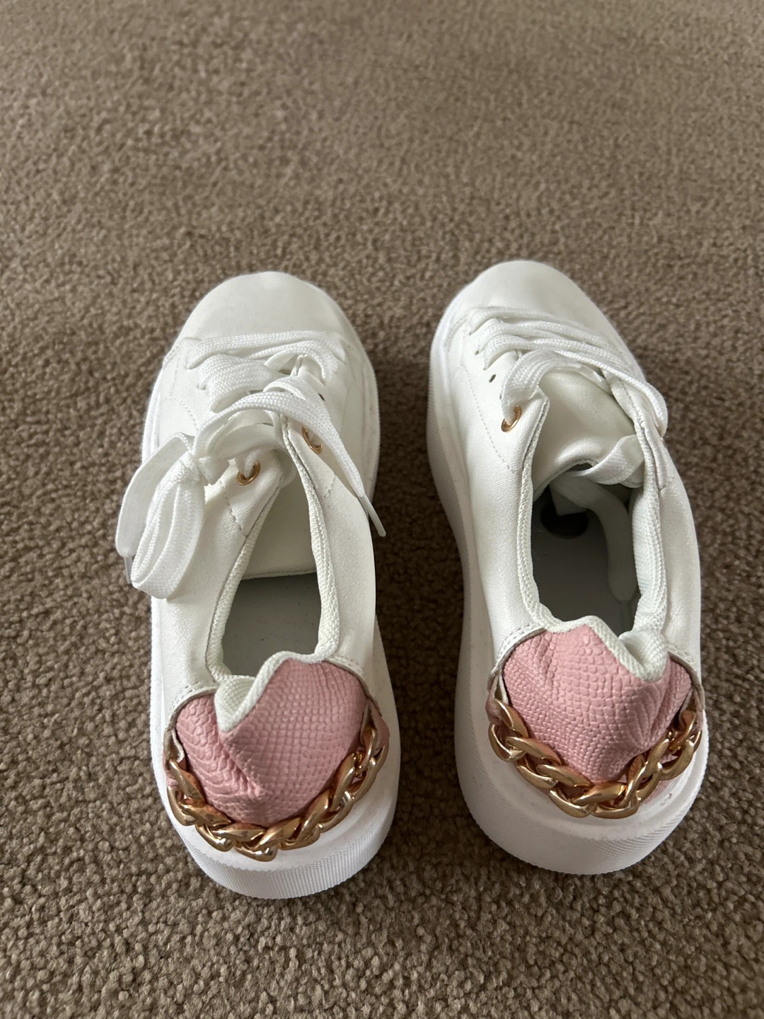 White fashion sneakers with pink accents and gold chain detail