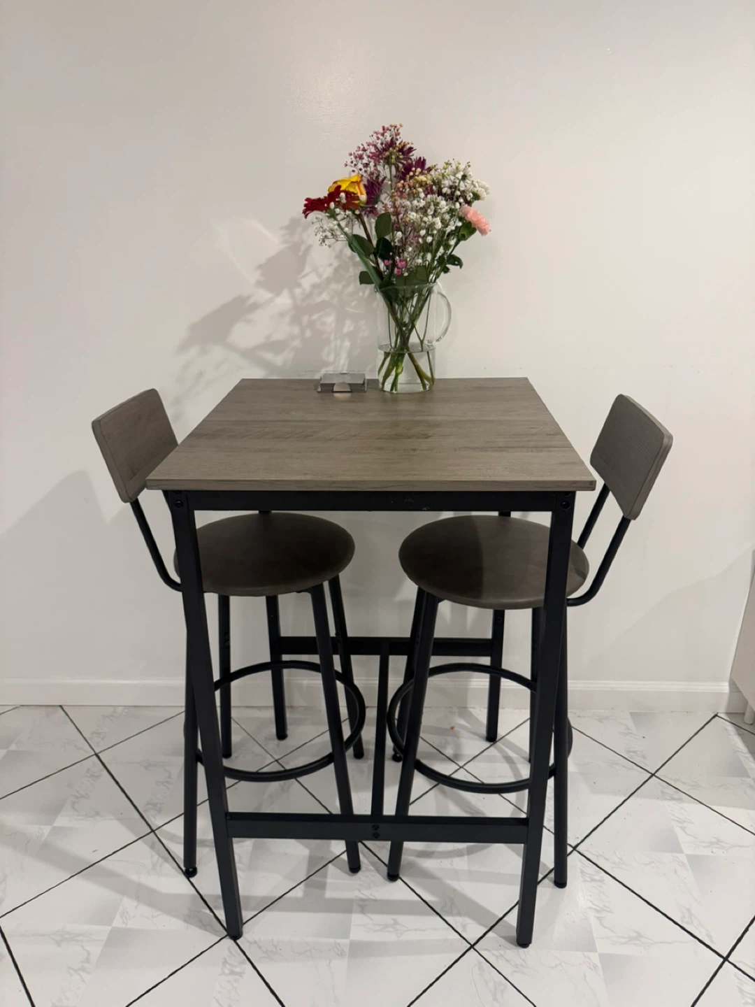 Bar height dining set with square table and 2 cushioned stools.