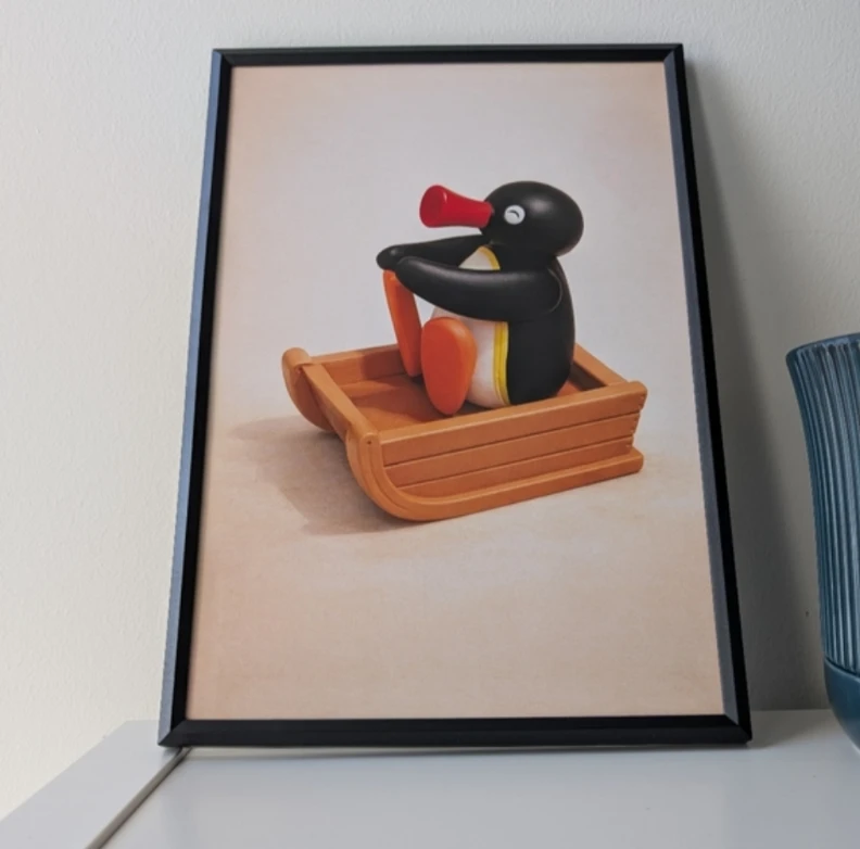 Framed Pingu on a Sled print in black frame 20x30 cm