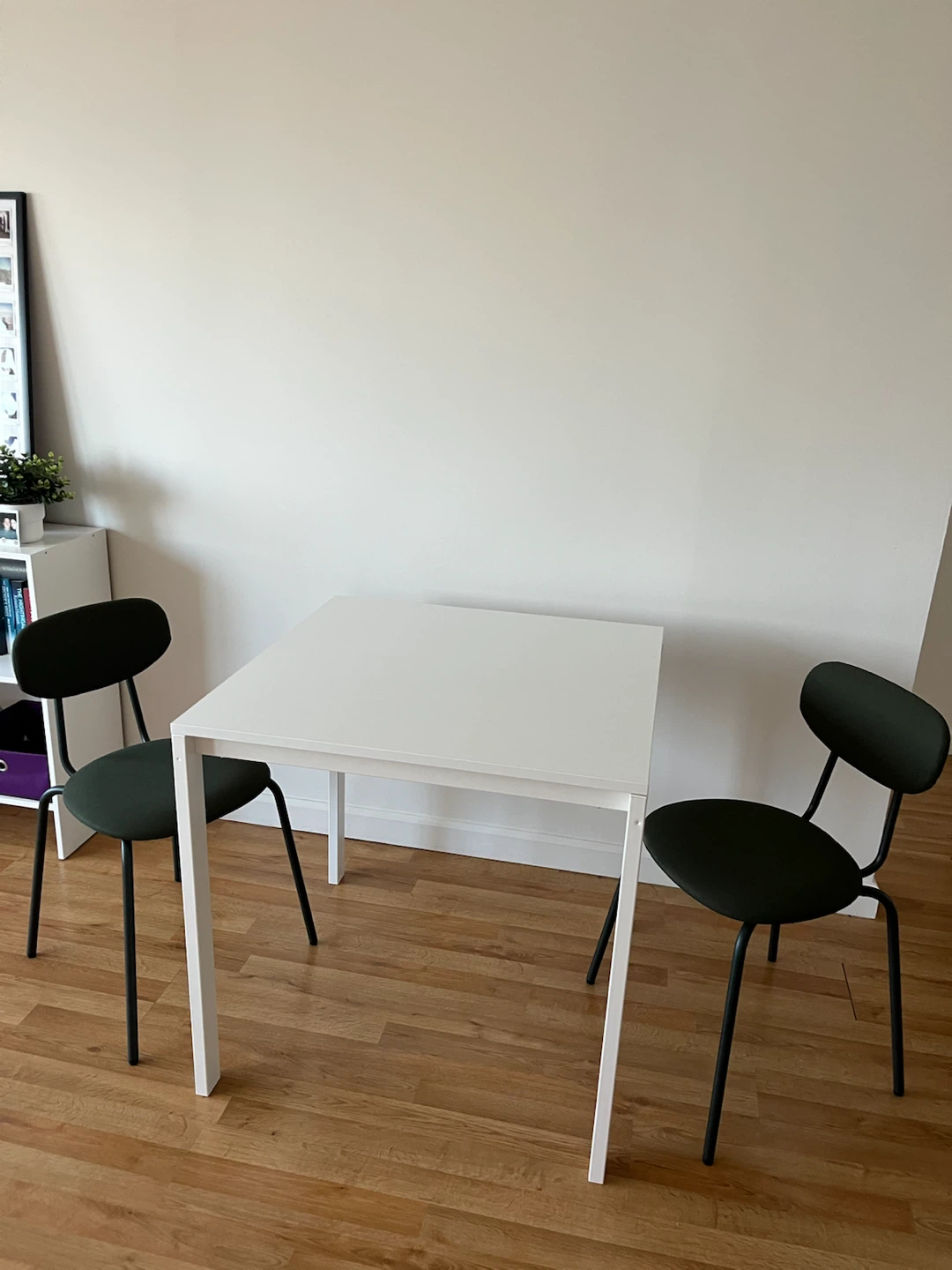 White dinning table with two dark green chairs