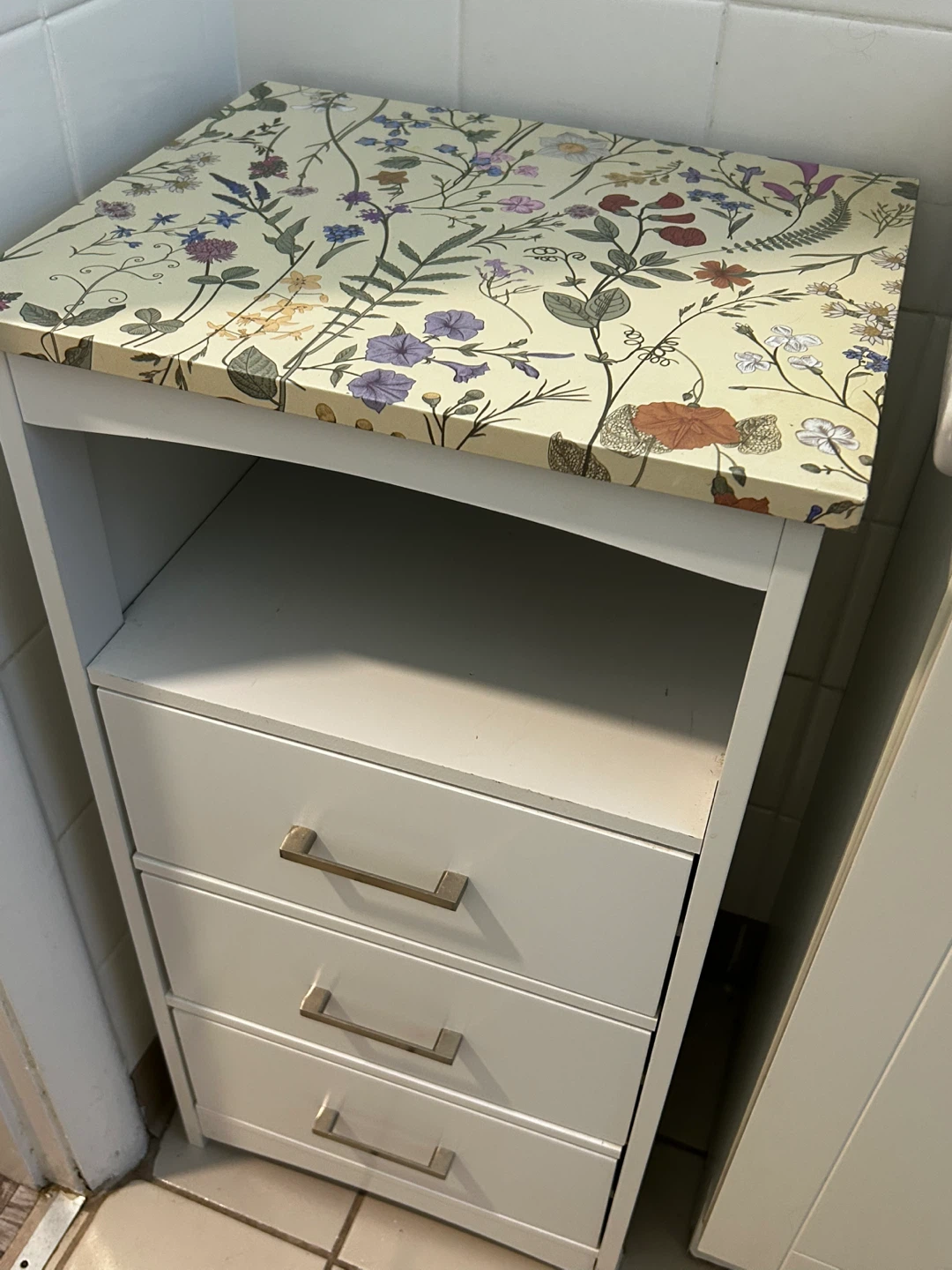 White bathroom cabinet with three drawers and floral top