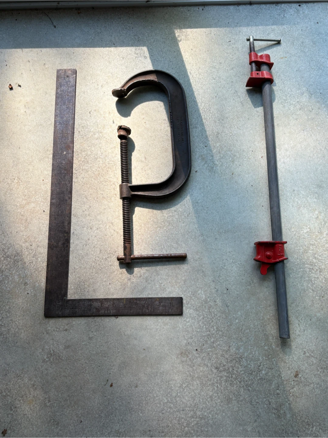 Vintage tool set: pipe clamp, C-clamp, and framing square